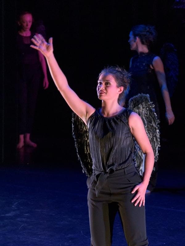 Een danser die een raaf voor moet stellen in zwarte kleding en zwarte vleugels. 
