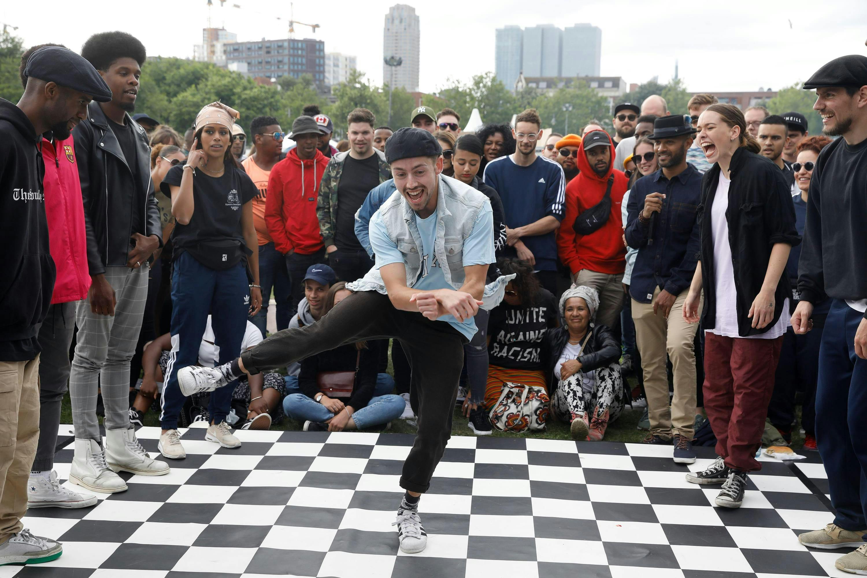 Een hiphop-danser op een zwart-wit geblokte dansvloer, omringd door publiek.