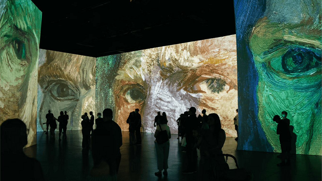 Mensen lopen rond in een tentoonstelling. Ze kijken naar digitale projecties van Von Gogh kunstwerken.