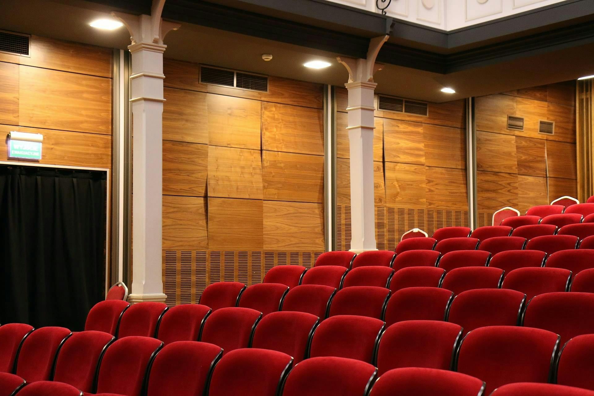 Detail van een lege theaterzaal, diverse rijen stoelen en de zijwand