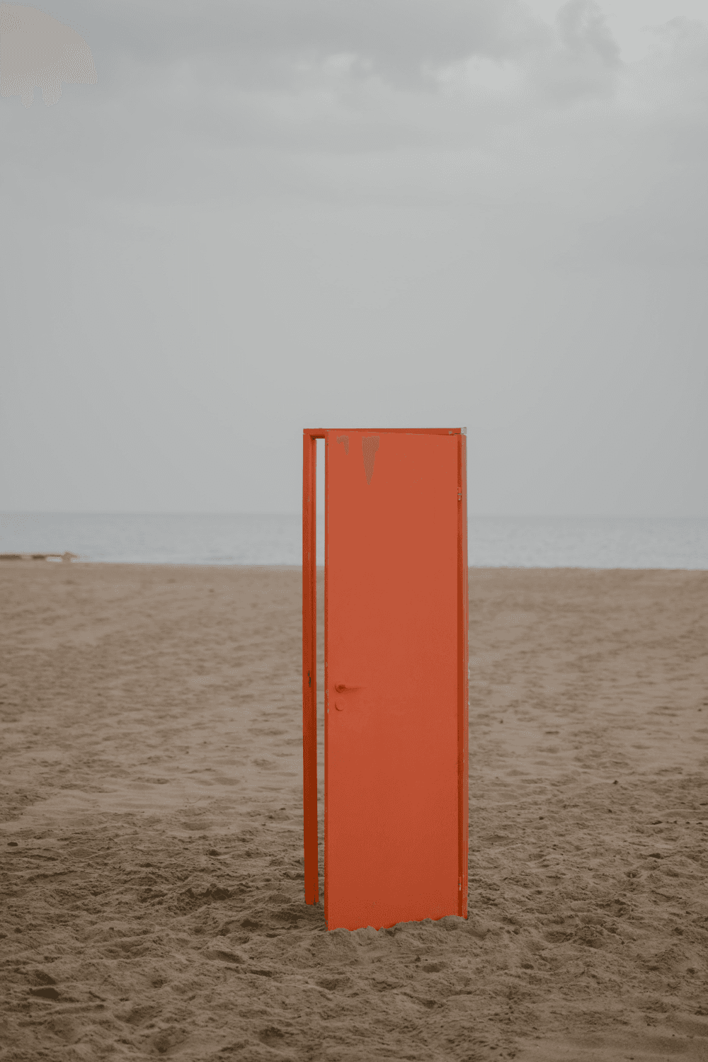Oranje deur staat rechtop op het strand. De deur staat op een heel klein kiertje.
