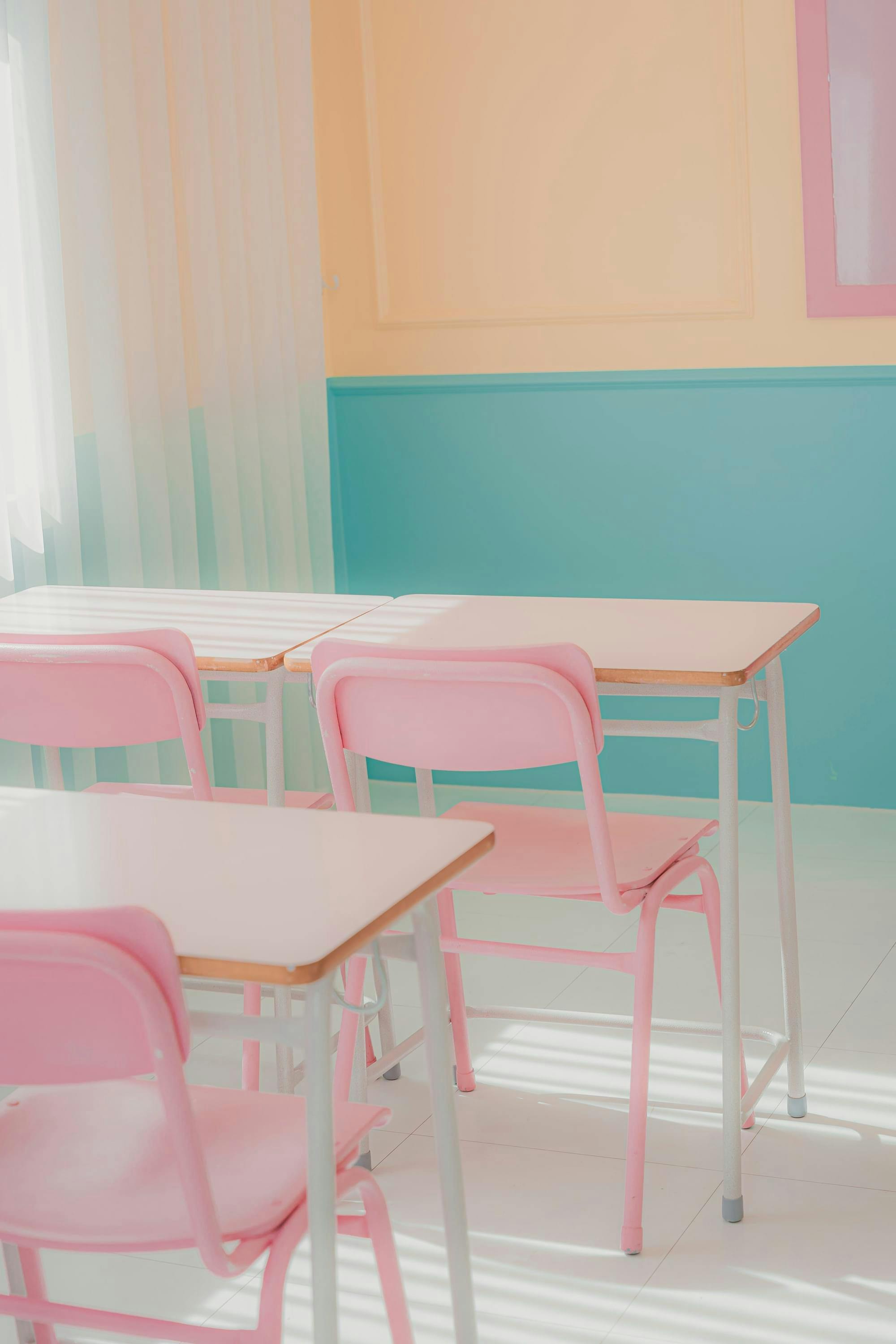 Pastelkleurig klaslokaal met 3 tafels en 3 roze stoelen.
