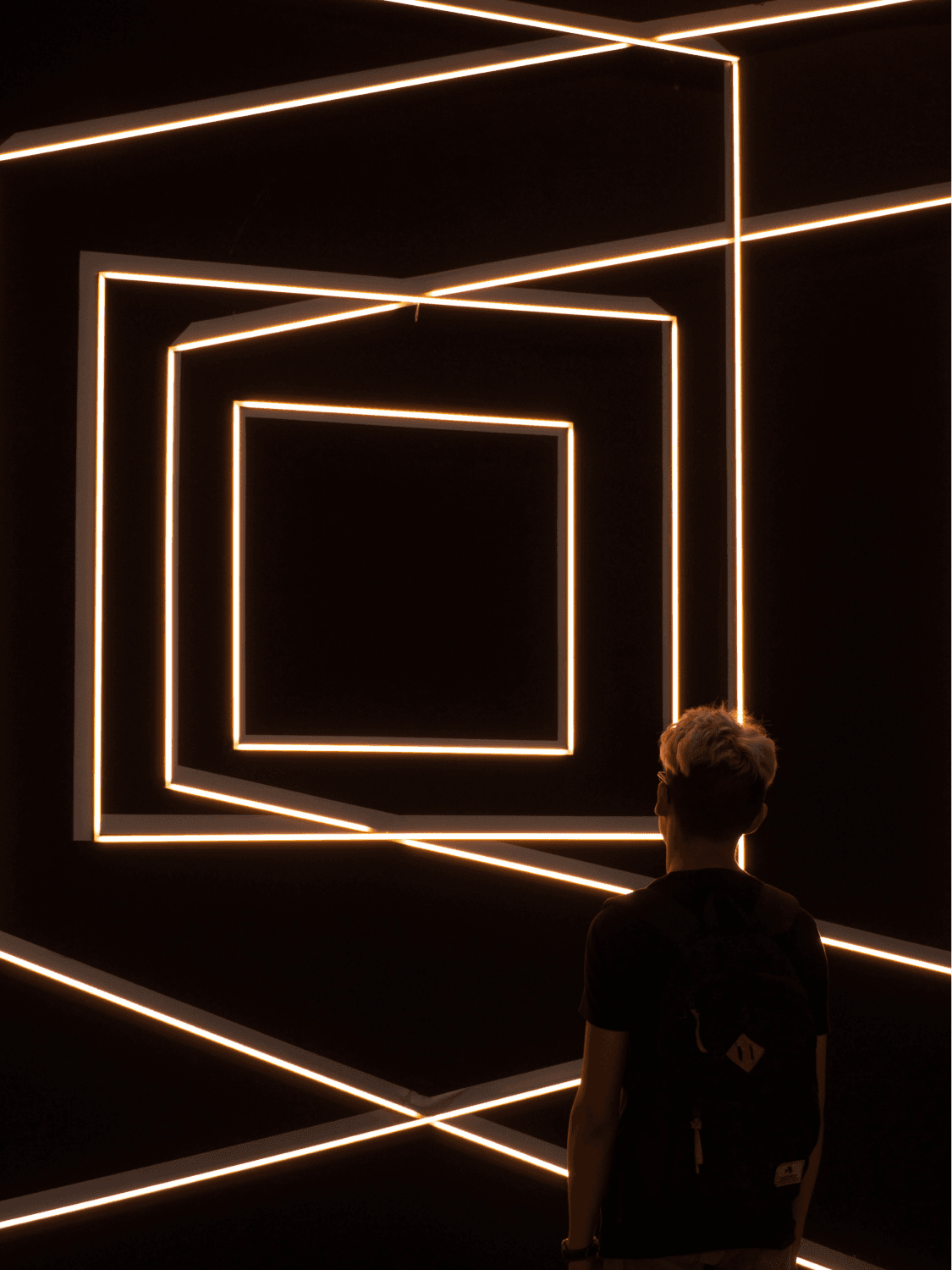 Persoon kijkt in een donkere ruimte naar een lichtinstallatie van vierkanten die elkaar doorkruisen.