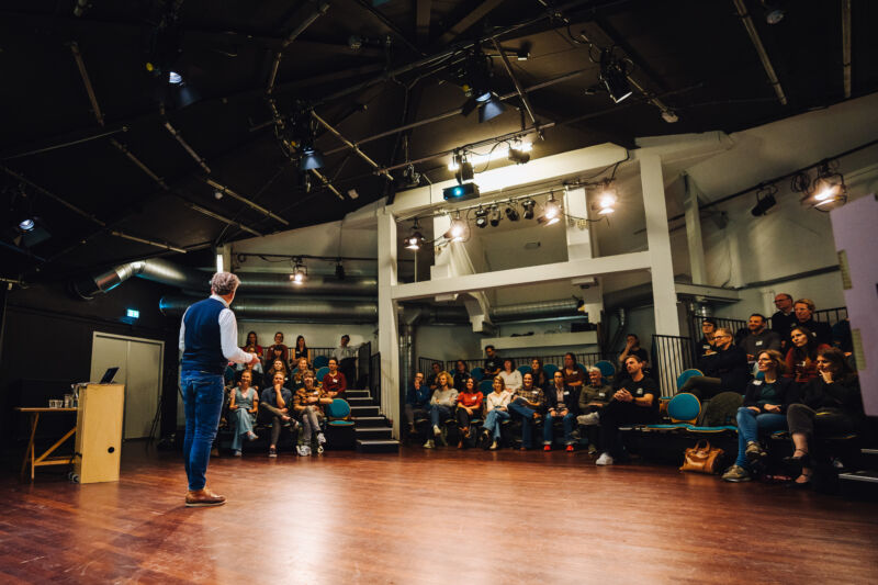 Foto van Micha Bruinvels die aan het presenteren is op de DEN Community meet-up. Op de voorgrond zie je Micha, daarachter de deelnemers in het publiek