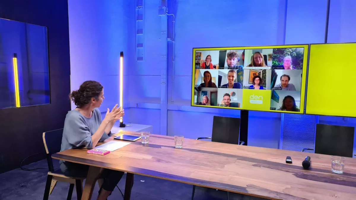 DEN directeur Maaike Verberk zit aan een tafel en spreekt een online publiek toe tijdens de Digitale transformatie conferentie.