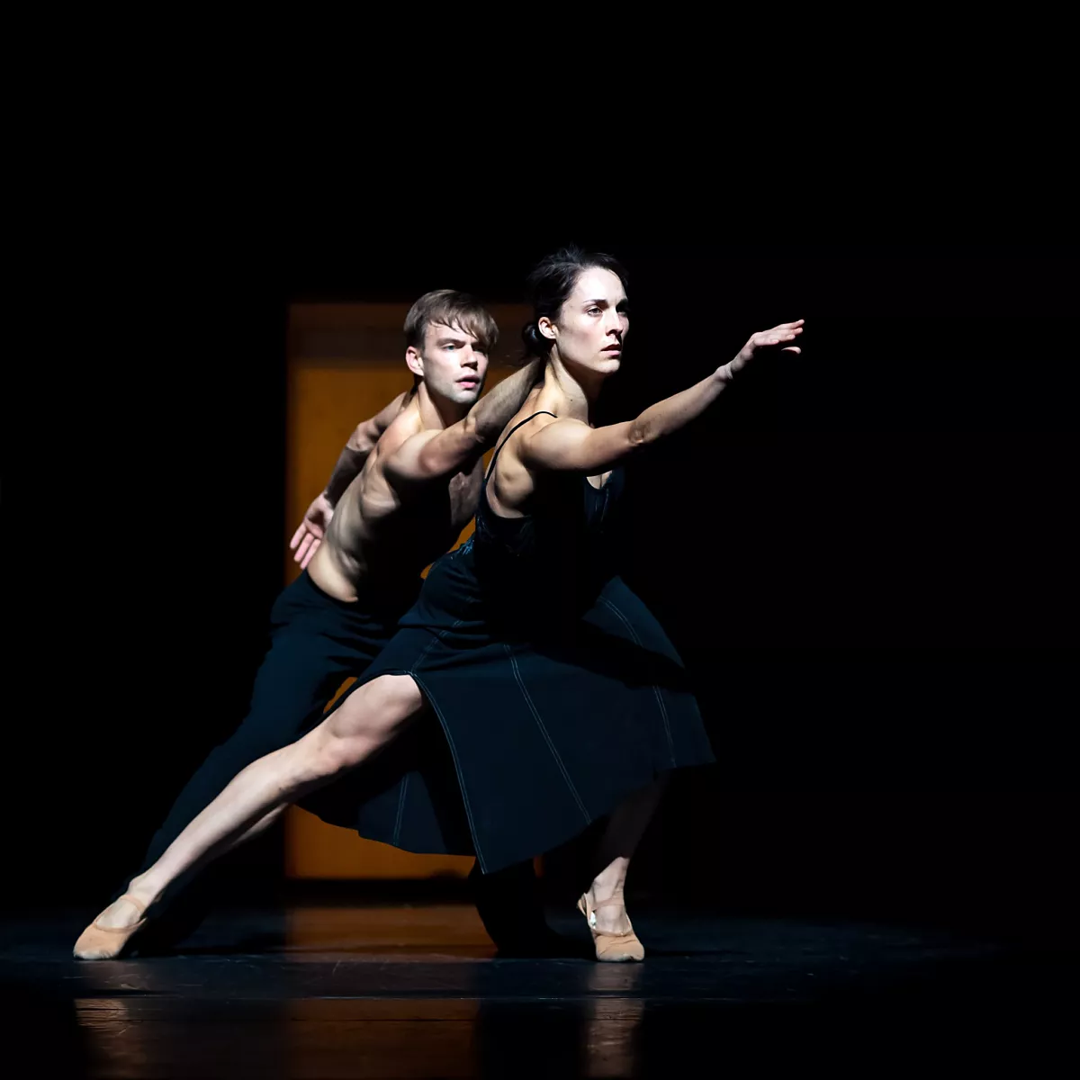 Twee dansers. De voorste danser lijkt een vrouw en draagt een zwart kort jurkje, ze staat in een lunge met een been gestrekt en de ander gebogen. Haar arm is uitgestrekt naar boven voor haar gezicht. Op haar schouder leunt een mannelijk uitziende danser met ontbloot bovenlichaam. Hij volgt haar blik en uitgestrekte arm.
