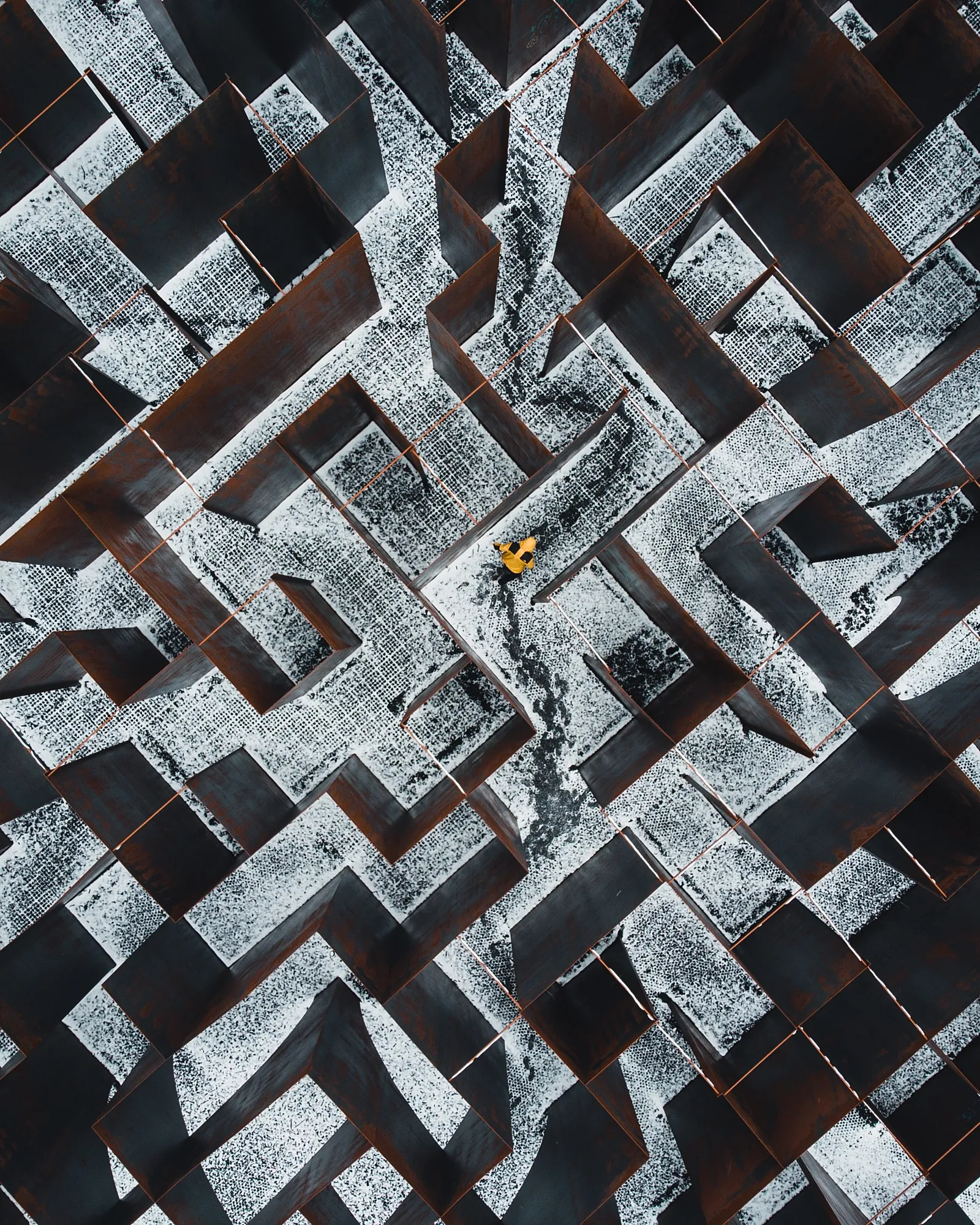 Maze seen from above. Through the maze walks someone with a bright yellow coat.
