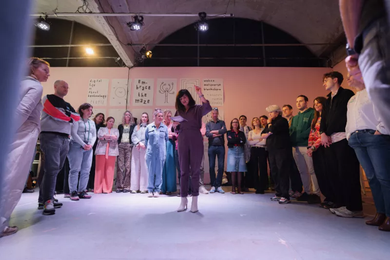 Een groep kunstprofessionals in een kring rondom Anic van Damme