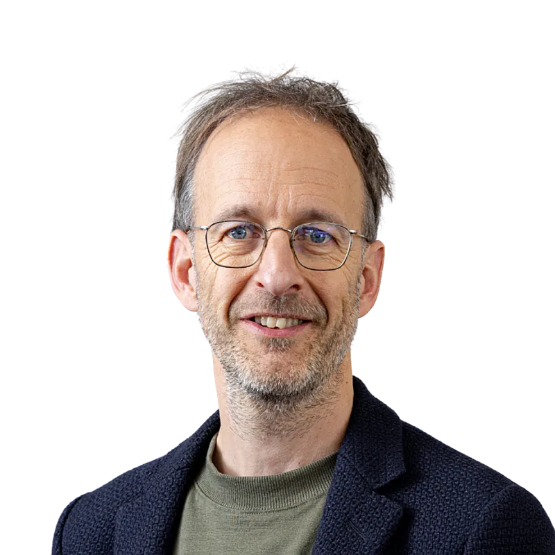 Portretfoto van Erik. Een man met een ronde bril, kort haar en een stoppelbaard. Hij draagt een groen t-shirt en een donkerblauw jasje.