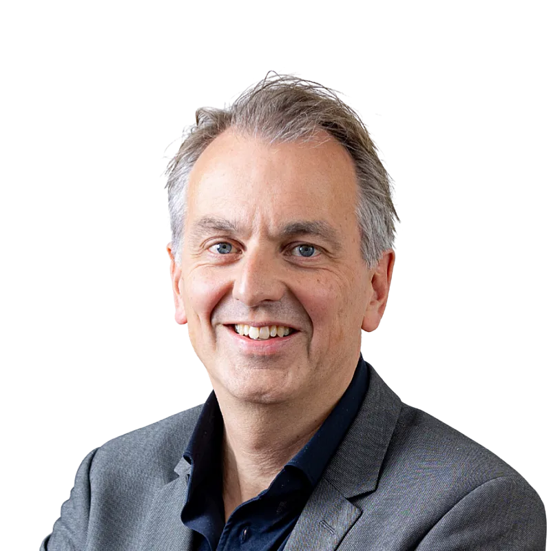 Portretfoto van Lucien Brouwer. Een man met kort grijs haar. Hij draagt een zwart overhemd en een grijs jasje.