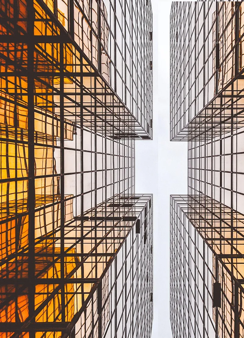 Doorkijkje tussen twee hoge gebouwen met oranje en glas. Perspectief is vanaf de grond omhoog kijkend.