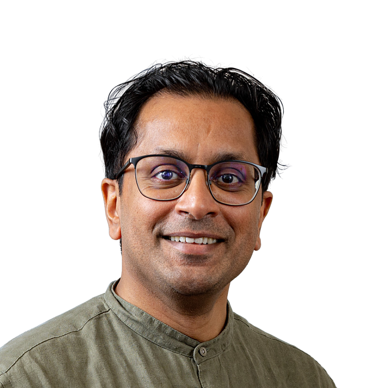 Portretfoto van een man met zwart haar en een zwarte bril. Hij draagt een groene blouse.