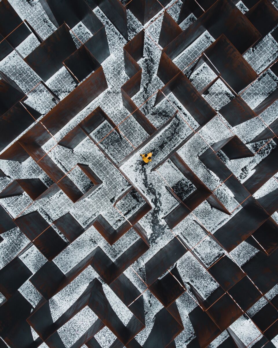 Maze seen from above. Through the maze walks someone with a bright yellow coat.