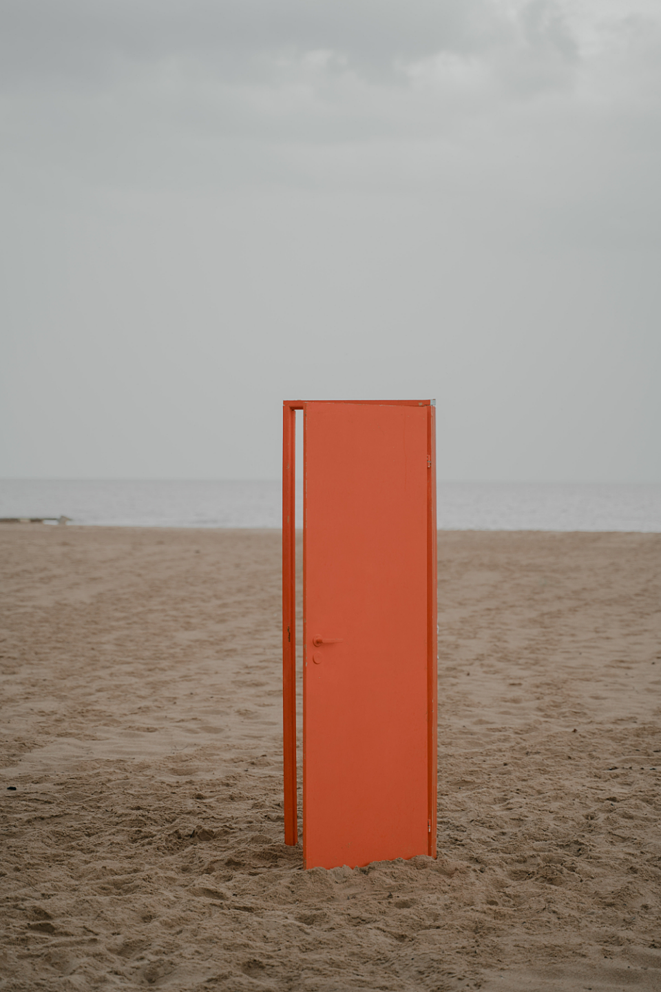 Orange door standing upright on the beach. The door is ajar.